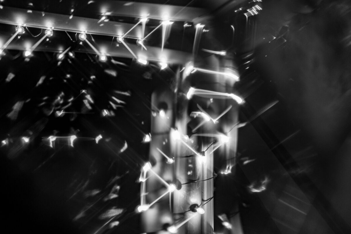 "Light Streaks" ©Zach Dobson Top 10 Photos 2024  Holiday lights in black & white viewed through window with beveled glass. Carmel, Indiana.