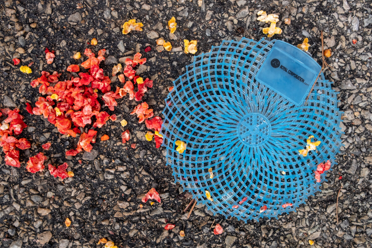 "Blue Disc, Red Popcorn" ©Zach Dobson Top 10 Photos 2024  Blacktop with blue circle plastic trash and red and yellow popcorn. Indianapolis, Indiana