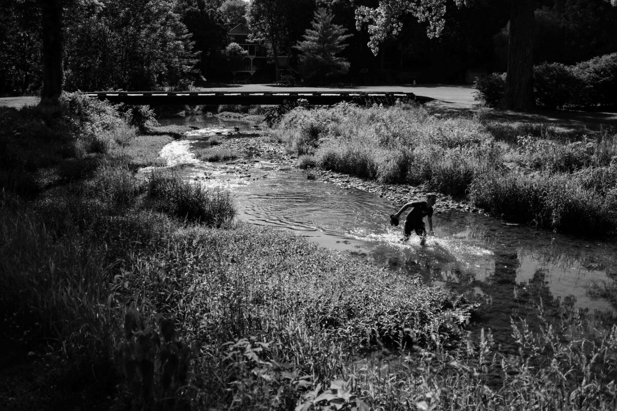 a kid in a creek on a golf course looking for lost golf balls