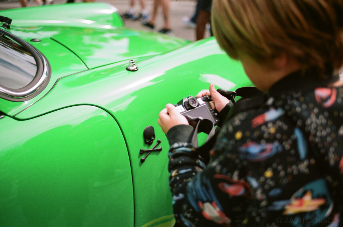 A child photographs a skull and crossbones emblem on the side of a bright green Porsche at Carmel Artomobilia 2024