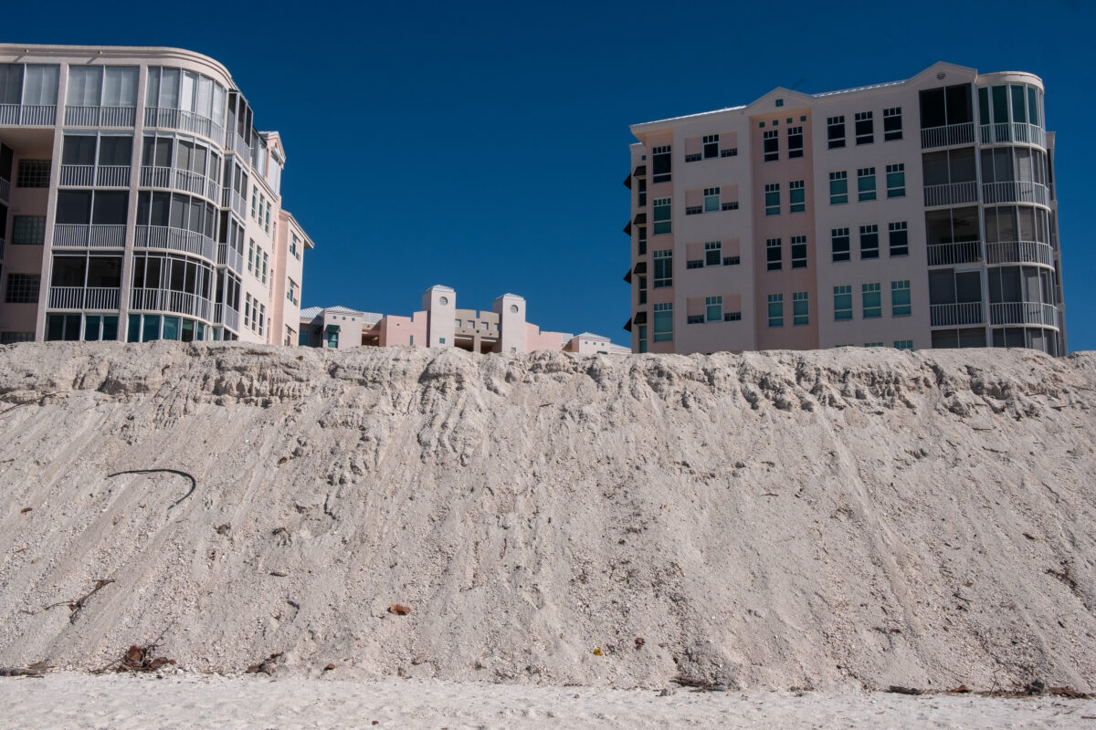 Sand dune in front of coral colored condo buildings. Bonita Springs, Florida.