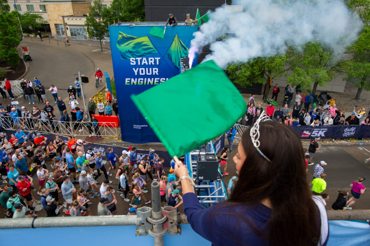 Above the starting line, waving the green flag at the 2025 Indiana University Health 500 Festival Mini Marathon in Indianapolis
