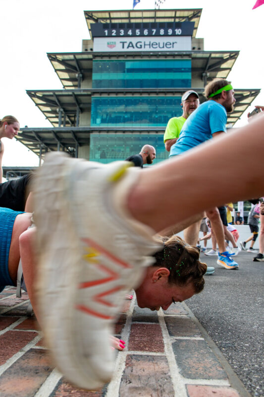 Runners stop to kiss the bricks at the Indianapolis Motor Speedway track during the 2025 Indiana University Health 500 Festival Mini Marathon in Indianapolis