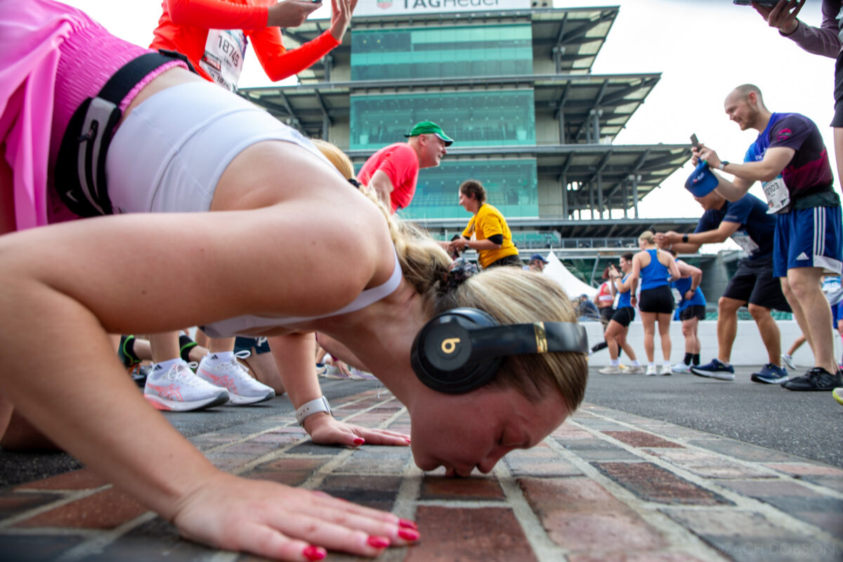 Runners stop to kiss the bricks at the Indianapolis Motor Speedway track during the 2025 Indiana University Health 500 Festival Mini Marathon in Indianapolis