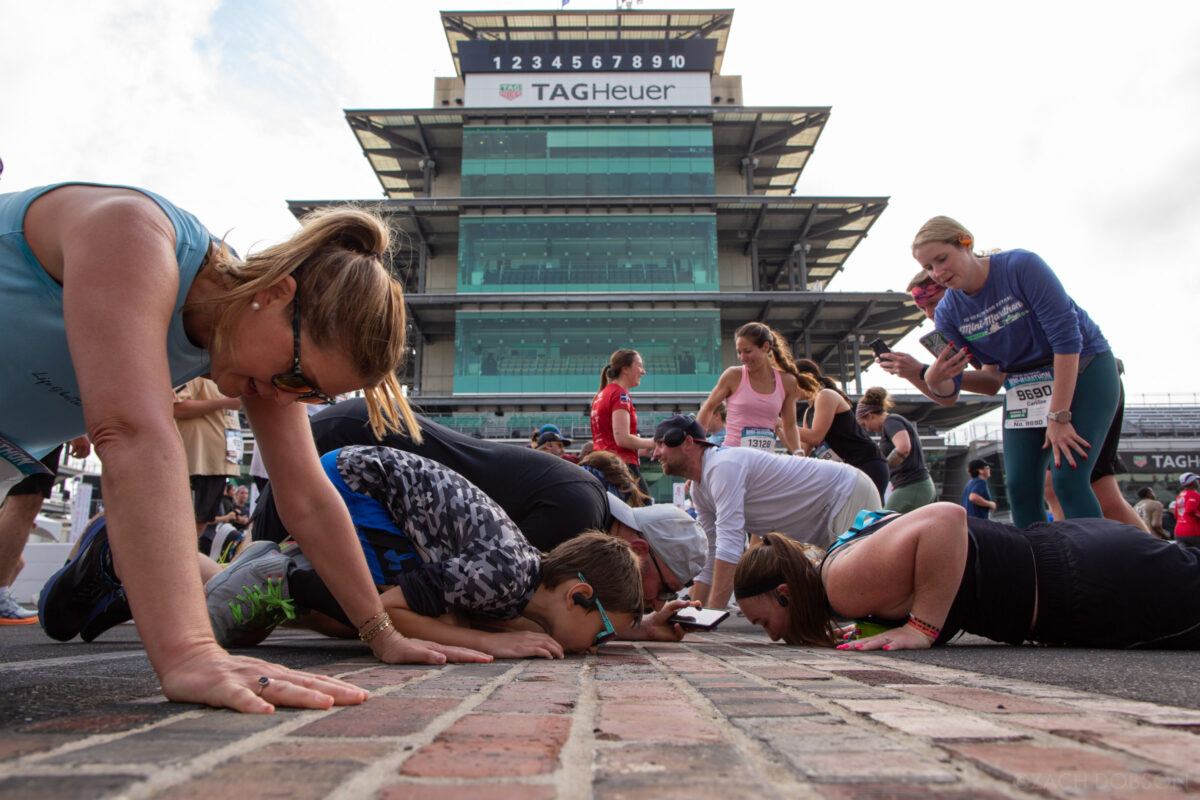 Runners stop to kiss the bricks at the Indianapolis Motor Speedway track during the 2025 Indiana University Health 500 Festival Mini Marathon in Indianapolis