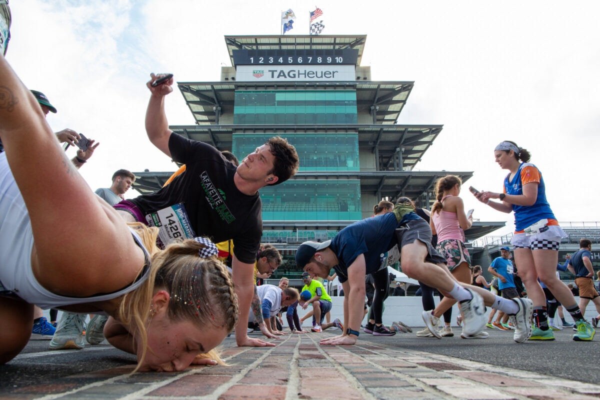 Runners stop to kiss the bricks at the Indianapolis Motor Speedway track during the 2025 Indiana University Health 500 Festival Mini Marathon in Indianapolis